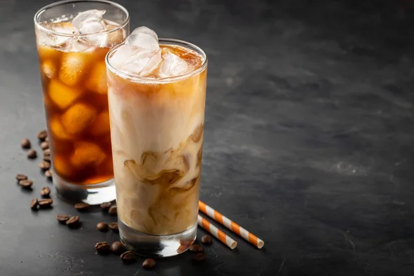 Es kopi dalam gelas tinggi dengan krim dituangkan di atas, gula coklat dan biji kopi. Minuman musim panas yang dingin dengan latar belakang yang gelap. Dengan ruang fotokopi — Stok Foto