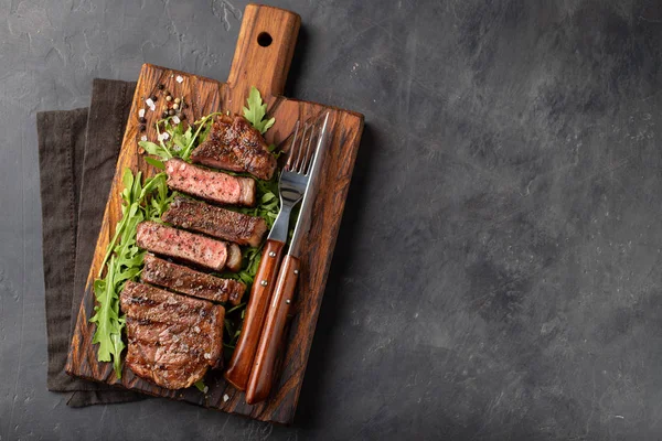 Gros plan prêt à manger steak New York races de bœuf d'Angus noir avec des herbes, de l'ail et du beurre sur une planche de bois. Le plat fini pour le dîner sur un fond de pierre sombre. Vue supérieure avec espace de copie — Photo