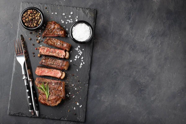 Closeup pronto para comer bife Nova York raças de carne de Angus preto com ervas, alho e manteiga em uma placa de pedra. O prato terminado para o jantar em um fundo de pedra escura. Vista superior com espaço de cópia — Fotografia de Stock