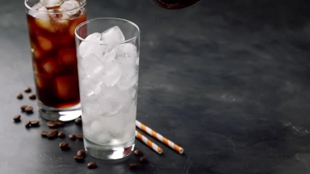 Two glasses of cold coffee on a dark background. In a tall glass with ice pour black coffee. slow motion — Stock Video
