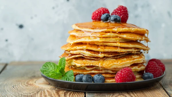 Primer plano deliciosos panqueques, con arándanos frescos, frambuesas y miel sobre un fondo claro. Con espacio de copia — Foto de Stock