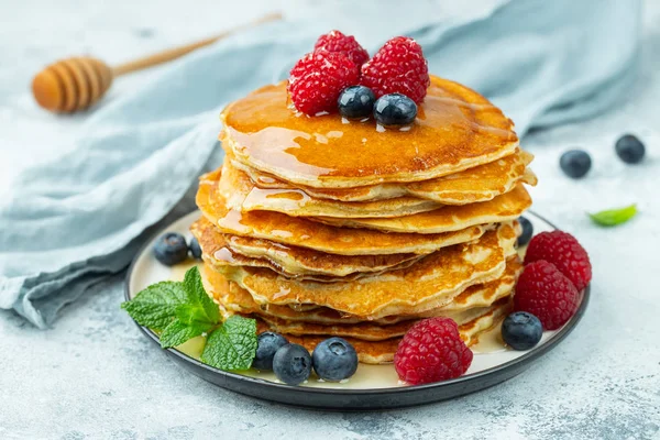 Primeros planos deliciosos panqueques, con arándanos frescos, frambuesas y miel sobre un fondo claro — Foto de Stock