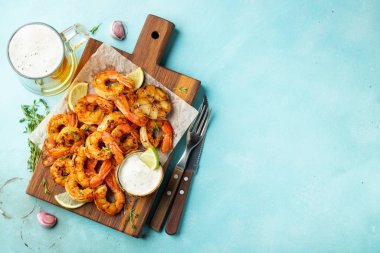 Açık mavi beton zemin üzerinde limon, sarımsak ve sosla servis edilen ızgara karides şişleri veya langoustinler. Deniz ürünleri ve bira. Kopyalama alanı olan üst görünüm. Düz yatıyordu