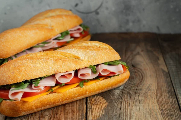 Дві довгі бутерброди з руколою, скибочки свіжих помідорів, шинка та сир — стокове фото