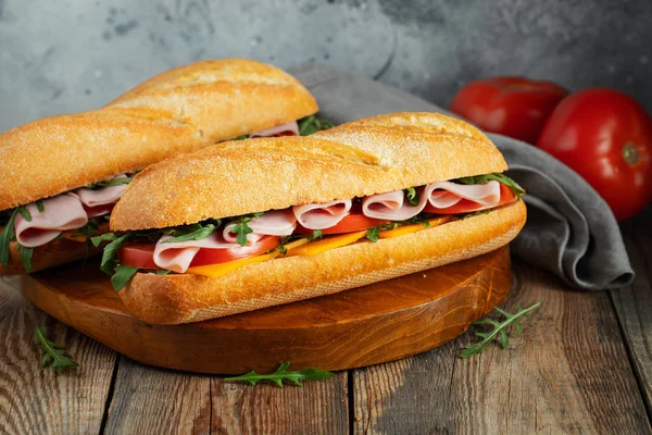Дві довгі бутерброди з руколою, скибочки свіжих помідорів, шинка та сир — стокове фото