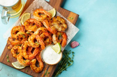 Açık mavi beton zemin üzerinde limon, sarımsak ve sosla servis edilen ızgara karides şişleri veya langoustinler. Deniz ürünleri ve bira. Kopyalama alanı olan üst görünüm. Düz yatıyordu