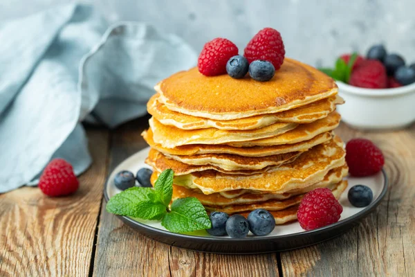 Deliciosos panqueques de cerca, con arándanos frescos, frambuesas y miel sobre un fondo claro — Foto de Stock