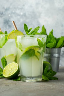 İki ev yapımı limonata ya da mojito kokteyli, limon, nane şekeri ve buz küpleriyle birlikte, hafif taş bir masanın üzerinde. Taze yaz içeceği..