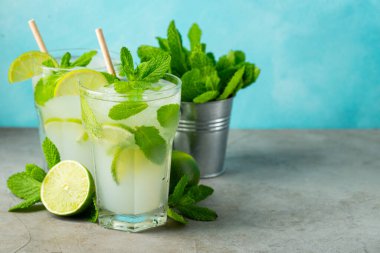 İki ev yapımı limonata ya da mojito kokteyli, limon, nane şekeri ve buz küpleriyle birlikte, hafif taş bir masanın üzerinde. Taze yaz içkisi. Kopyalama alanı ile.