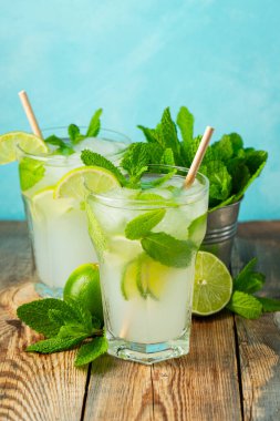 İki ev yapımı limonata ya da mojito kokteyli, limon, nane ve buz küpleri ahşap bir kırsal masada bir bardakta. Taze yaz içeceği..