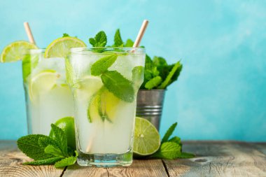 İki ev yapımı limonata ya da mojito kokteyli, limon, nane ve buz küpleri ahşap bir kırsal masada bir bardakta. Taze yaz içkisi. Kopyalama alanı ile.
