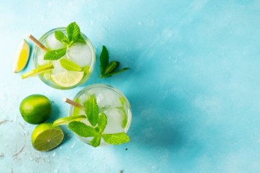 İki ev yapımı limonata ya da mojito kokteyli, limon, nane şekeri ve buz küpleriyle birlikte, hafif taş bir masanın üzerinde. Taze yaz içkisi. Kopyalama alanı olan üst görünüm.