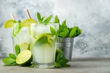 İki ev yapımı limonata ya da mojito kokteyli, limon, nane şekeri ve buz küpleriyle birlikte, hafif taş bir masanın üzerinde. Taze yaz içkisi. Kopyalama alanı ile