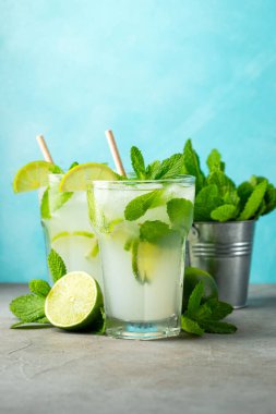 İki ev yapımı limonata ya da mojito kokteyli, limon, nane şekeri ve buz küpleriyle birlikte, hafif taş bir masanın üzerinde. Taze yaz içeceği.