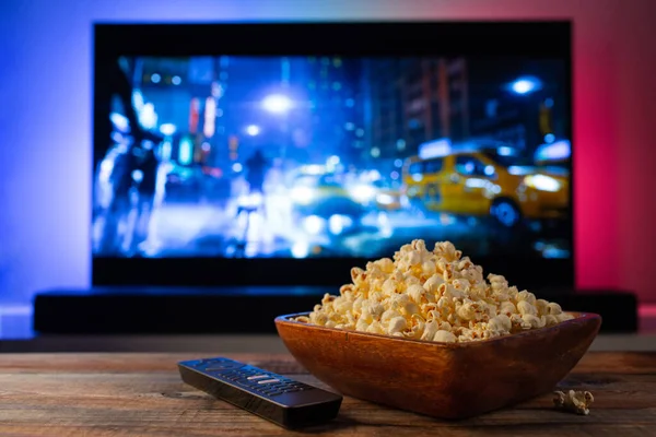 Arkaplanda bir kase patlamış mısır ve uzaktan kumanda var. Televizyon çalışıyor. Akşam sıcacık, evde film ya da TV dizisi seyrediyor..