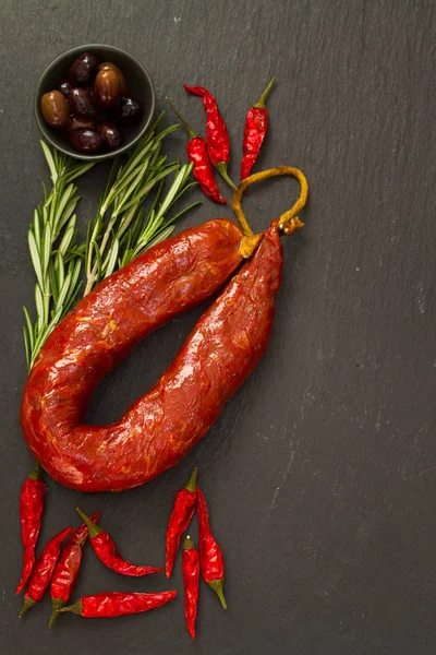 Smoked sausage with olives and herbs on black background — Stock Photo, Image