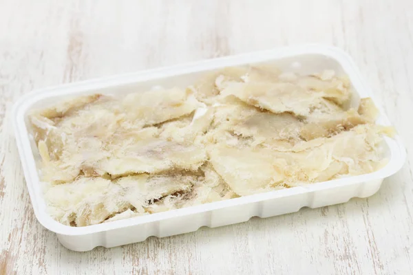 Salted codfish on plastic dish on white wooden background — Stock Photo, Image