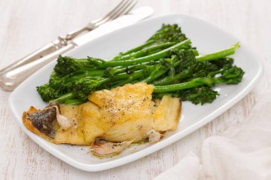 Kızarmış Morina balığı beyaz tabakta yeşillikleri ile