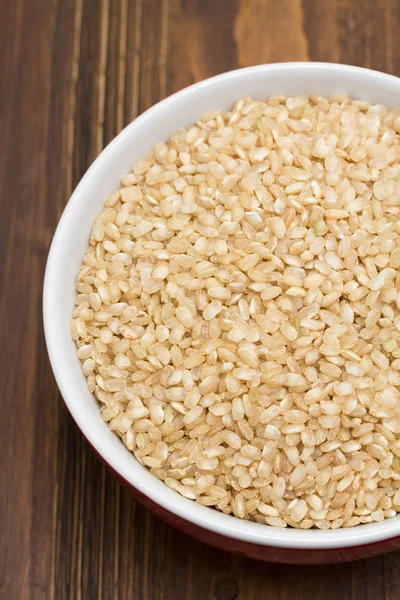 Raw rice in red bowl on wooden background — Stock Photo, Image