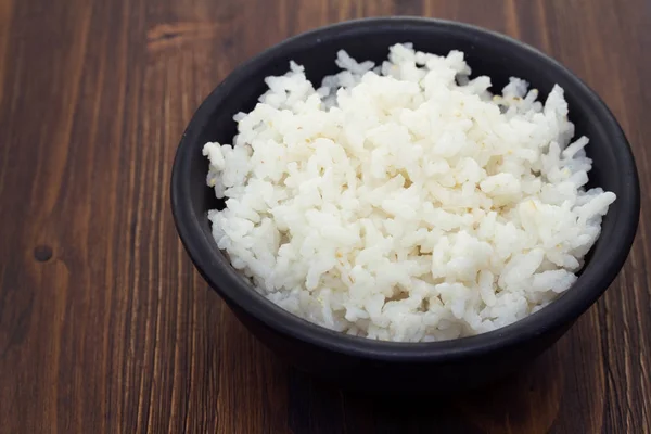 Boiled rice in black bowl in wooden background — Stock Photo, Image