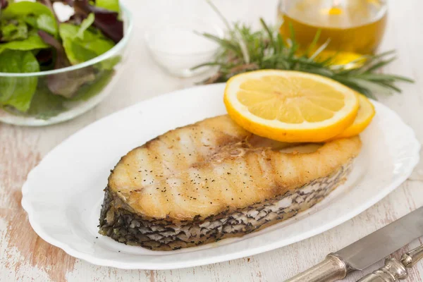 Pescado a la parrilla con limón en plato blanco sobre fondo de madera —  Fotos de Stock