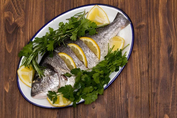 Roher Fisch mit Kräutern und Zitrone auf Teller auf Holzgrund — Stockfoto