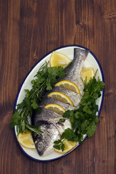 Roher Fisch mit Kräutern und Zitrone auf Teller auf Holzgrund — Stockfoto