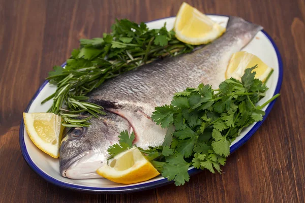 Roher Fisch mit Kräutern und Zitrone auf Teller auf Holzgrund — Stockfoto