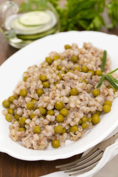 Buckwheat with peas on white dish on wooden background — Stock Photo, Image