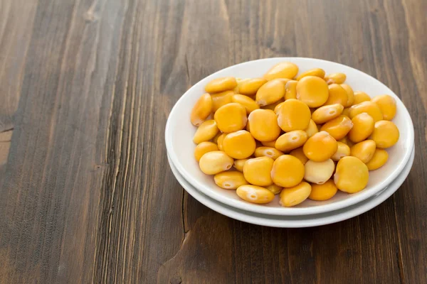 Altramuces salados sobre plato blanco sobre fondo marrón de madera — Foto de Stock