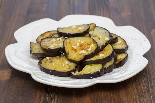 Melanzane fritte con aglio su piatto bianco su sfondo di legno — Foto Stock