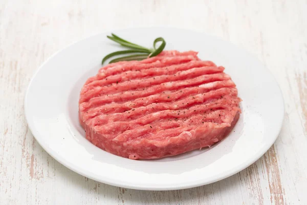 raw hamburger on white plate on wooden background