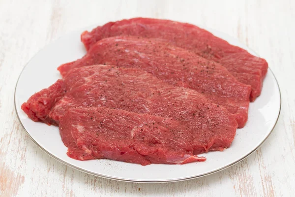 Surowe mięso na białym talerzu na podłoże drewniane — Zdjęcie stockowe