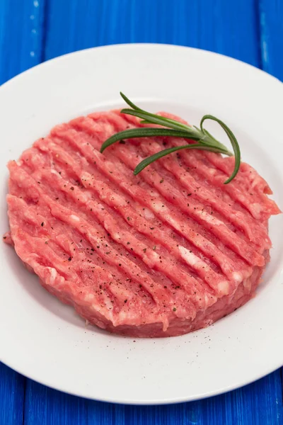 Hamburger crudo su piatto bianco su fondo di legno — Foto Stock