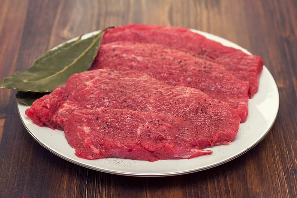Rauw vlees op witte plaat op houten achtergrond — Stockfoto