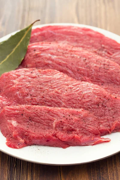 Carne cruda su piatto bianco su fondo di legno — Foto Stock