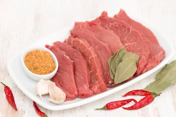 Raw meat with herbs on white dish on wooden background — Stock Photo, Image