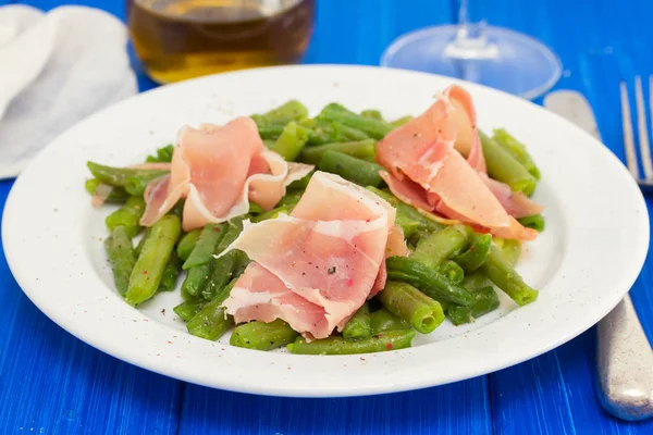 Green beans with prosciutto on white plate on wooden background — Stock Photo, Image