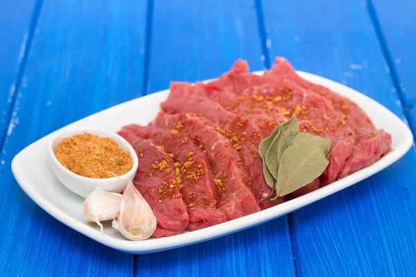 Rohes Fleisch mit Kräutern auf weißem Teller auf blauem Holzhintergrund — Stockfoto