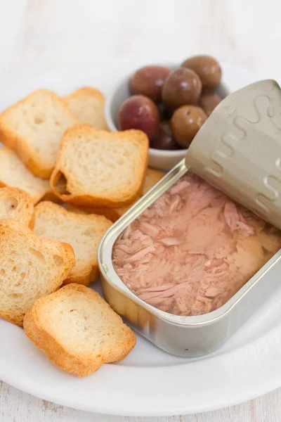 Atún en caja de hierro con tostadas y aceitunas en plato blanco —  Fotos de Stock