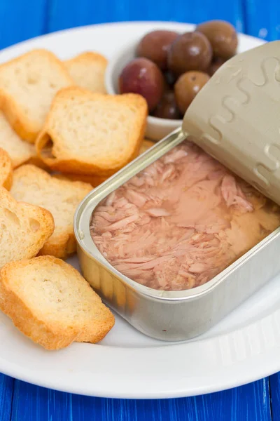 Тунец в железной коробке с тостами и оливками на белой тарелке — стоковое фото