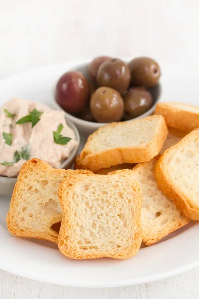 Тосты с рыбным паштетом и оливками на белой тарелке — стоковое фото