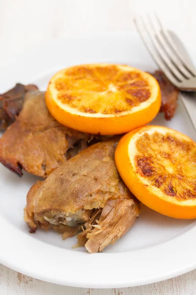 Запечённая утка с орангом на белом блюде с вилкой и ножом — стоковое фото
