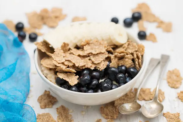 Flakes with blueberries and banana on brown bowl on wooden background — Stock Photo, Image