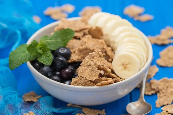 Flakes with blueberries and banana on brown bowl on wooden backg — Stock Photo, Image