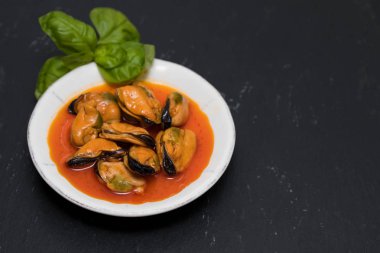 siyah arka plan üzerine beyaz çanak üzerinde soslu midye