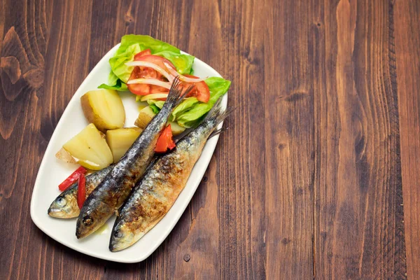 Sardinhas grelhadas com batata cozida e salada em prato branco — Fotografia de Stock