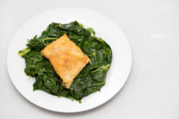 Жареная треска с зеленью на белой тарелке — стоковое фото