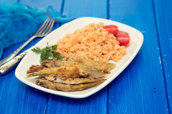 Éperlans frits avec riz tomate sur plat blanc sur fond bleu — Photo