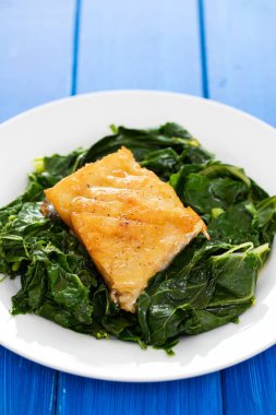 Kızarmış Morina balığı mavi zemin üzerine beyaz tabakta yeşillikleri ile